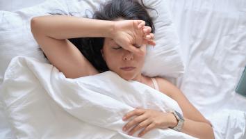 een vrouw in bed met de ogen dicht en een hand op haar voorhoofd