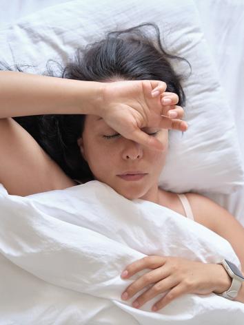 een vrouw in bed met de ogen dicht en een hand op haar voorhoofd