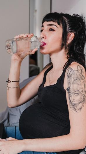 een zwangere vrouw drinkt uit een fles water