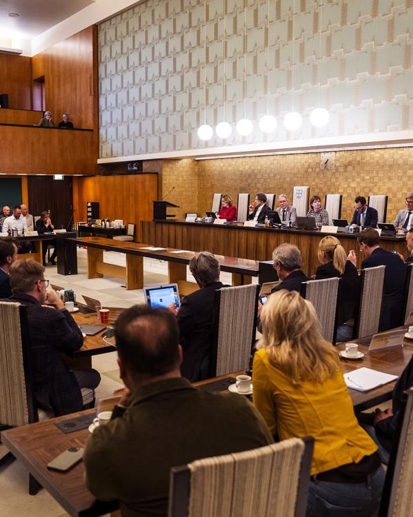 een vergadering in de raadszaal in gemeente Hilversum waar raadsleden en wethouders overleggen