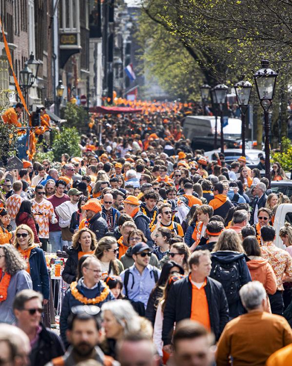 De Amsterdamse grachten vol met bootjes met mensen in oranje kleding