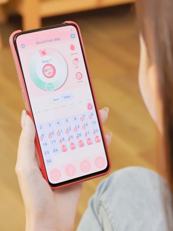een vrouw kijkt op haar telefoon naar een app die de menstruatiecyclus bijhoudt