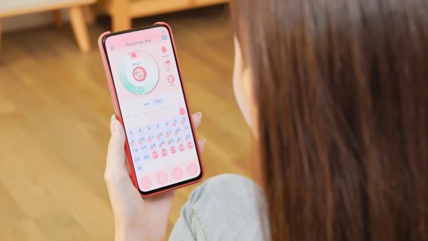 een vrouw kijkt op haar telefoon naar een app die de menstruatiecyclus bijhoudt