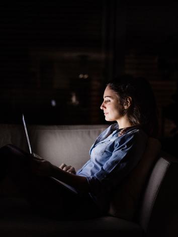 een vrouw kijkt in het donker op haar laptop