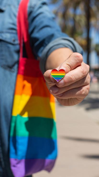 persoon toont regenbooghart-speld met diens Pride-tas op de achtergrond