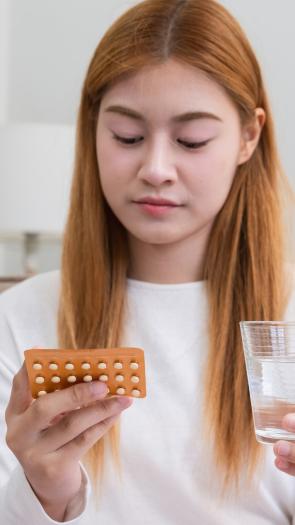 een vrouw kijkt naar een pillenstrip met een glas water in haar hand