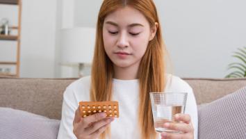 een vrouw kijkt naar een pillenstrip met een glas water in haar hand