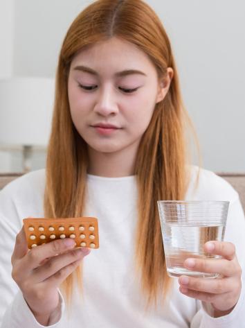 een vrouw kijkt naar een pillenstrip met een glas water in haar hand