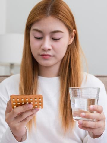 een vrouw kijkt naar een pillenstrip met een glas water in haar hand