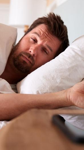 een man ligt in bed en kijkt vermoeid uit zijn ogen