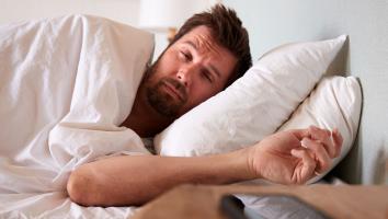 een man ligt in bed en kijkt vermoeid uit zijn ogen