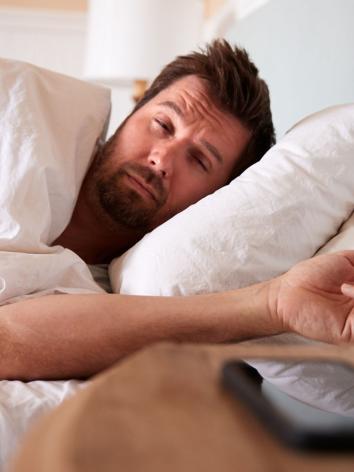 een man ligt in bed en kijkt vermoeid uit zijn ogen