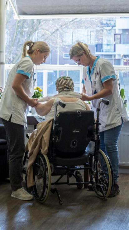 twee vrouwelijke zorgmedewerkers helpen een bewoner