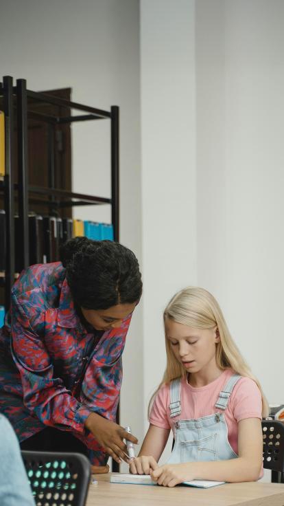 een vrouwelijke medewerker in het onderwijs legt iets uit aan een leerling