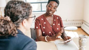Een man van kleur en een witte vrouw hebben een gesprek op werk.
