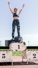 Vrouw in sportkleding staat juichend op de eerste plaats van een winnaarspodium