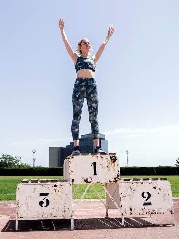 Vrouw in sportkleding staat juichend op de eerste plaats van een winnaarspodium