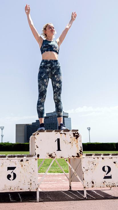 Vrouw in sportkleding staat juichend op de eerste plaats van een winnaarspodium