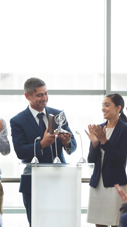Man in pak neemt prijs in ontvangst met applaudisserende collega's om hem heen