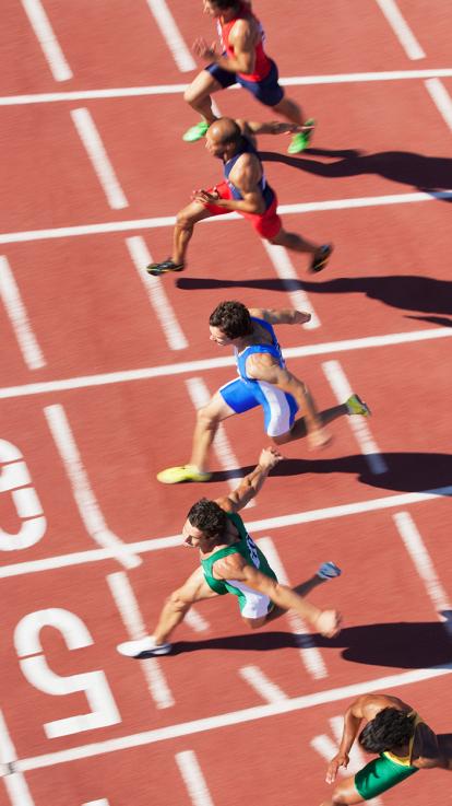 Een hardloopbaan van boven waar vijf mannen dicht bij elkaar finishen.