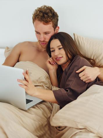 Man en vrouw liggen knuffelend in bed kijkend naar laptopscherm