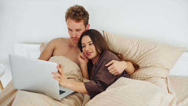Man en vrouw liggen knuffelend in bed kijkend naar laptopscherm