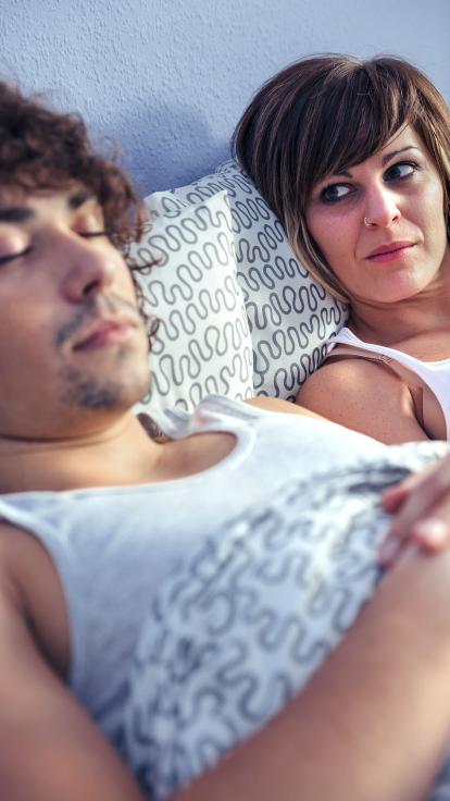 een vrouw kijkt naar haar slapende man in bed