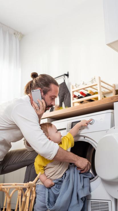 een man aan de telefoon terwijl hij de was doet met zijn kind