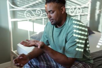 een man zit op bed en kijkt naar een pil in zijn hand