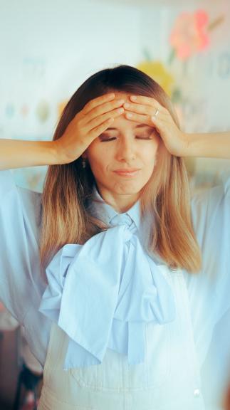 een vrouw met ogen dicht en handen op het voorhoofd in een drukke omgeving
