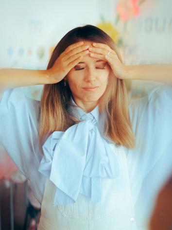 een vrouw met ogen dicht en handen op het voorhoofd in een drukke omgeving
