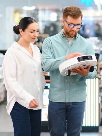 Een man en vrouw bekijken een robotstofzuiger in een winkel 