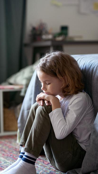 een kind zit naar beneden starend voor het bed