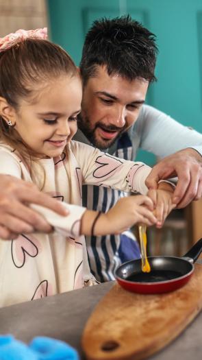 Vader en dochter breken samen een ei in een koekenpan