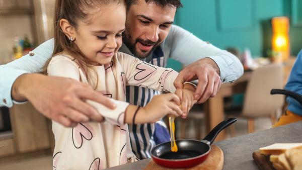 Vader en dochter breken samen een ei in een koekenpan