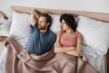 Een koppel ligt in bed. De man kijkt afwezig weg en de vrouw is ontevreden.