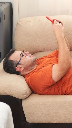 een man ligt op de bank en kijkt op zijn mobiel