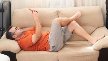 een man ligt op de bank en kijkt op zijn mobiel