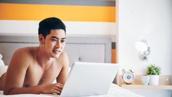 Man ligt zonder shirt op bed en bekijkt iets op zijn laptop