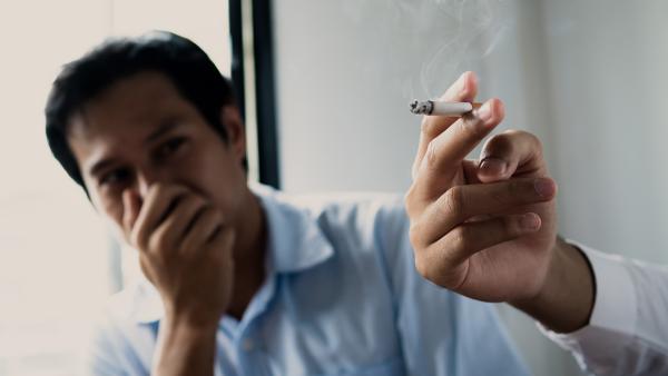 sigaret in iemands hand, iemand anders doet op de achtergrond een hand voor z'n mond