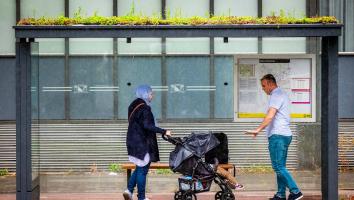 twee mensen staan te wachten bij een bushokje met een groen dak