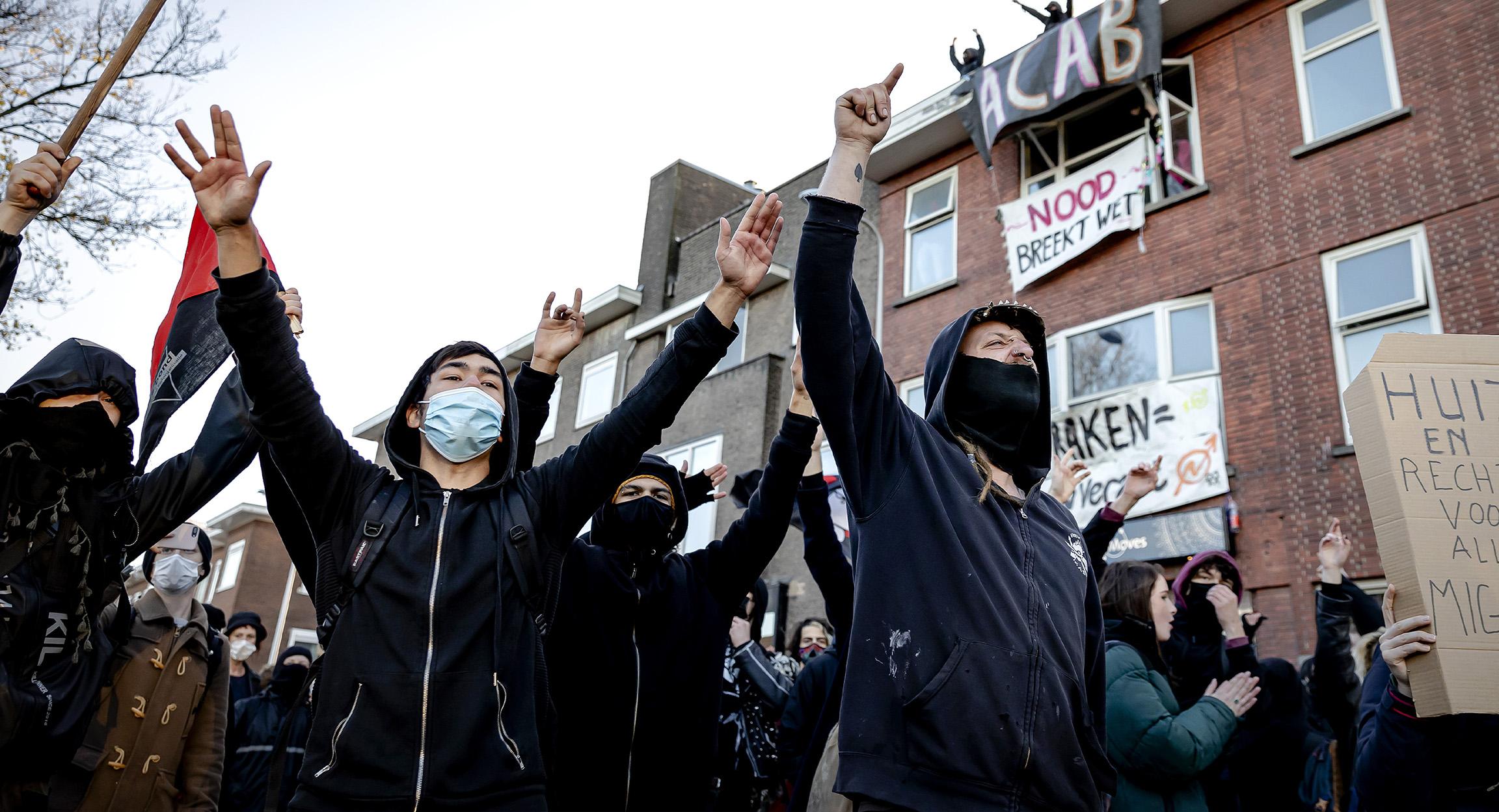 Mannen met gezichtsbedekking en capuchon staan met hun armen in de lucht op straat