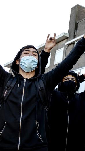 Mannen met gezichtsbedekking en capuchon staan met hun armen in de lucht op straat