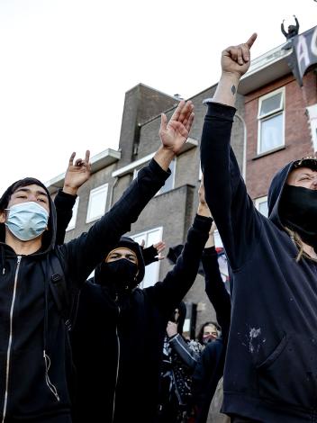 Mannen met gezichtsbedekking en capuchon staan met hun armen in de lucht op straat