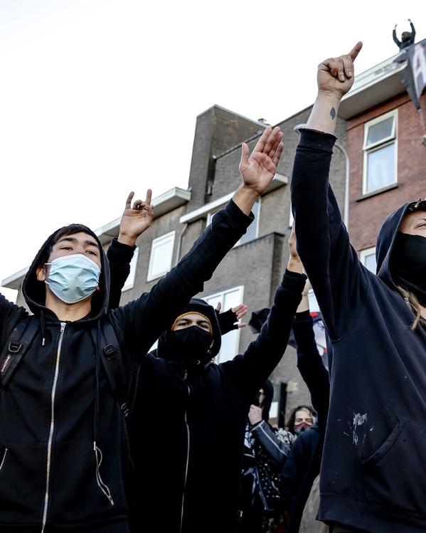 Mannen met gezichtsbedekking en capuchon staan met hun armen in de lucht op straat