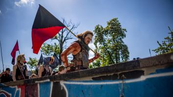 Man met verschillende kleuren bodypaint en een rood met zwart vlag op straat kijkt boos de camera in