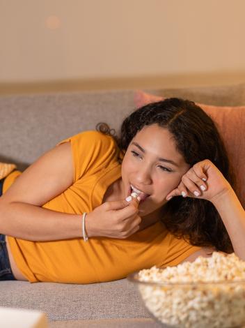 vrouw ligt op de bank en eet popcorn kijkend naar de tv