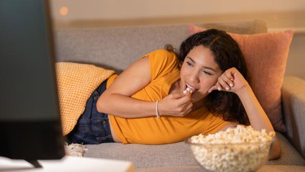 vrouw ligt op de bank en eet popcorn kijkend naar de tv