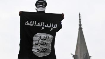 Man met hockeyhelm op houdt vlag met shahada ophoog naast een toren van een moskee