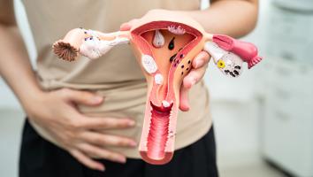een vrouw houdt haar hand op haar buik en in de andere hand houdt ze een baarmoeder-model vast